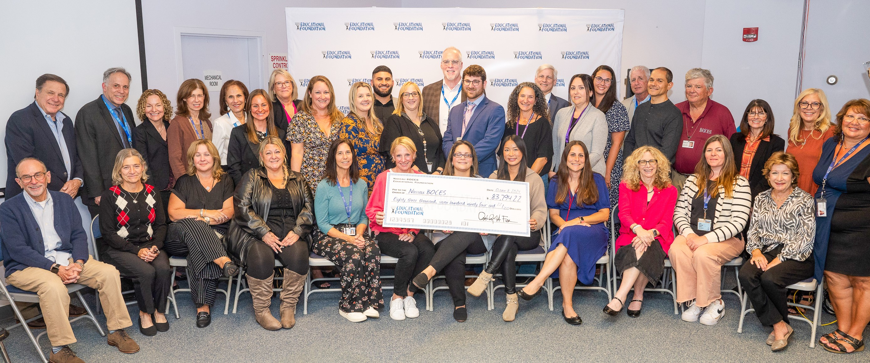  Group of smiling men and women with a large bank check in front of them for $83,794.22